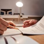 Hands reviewing and signing paperwork at a desk.